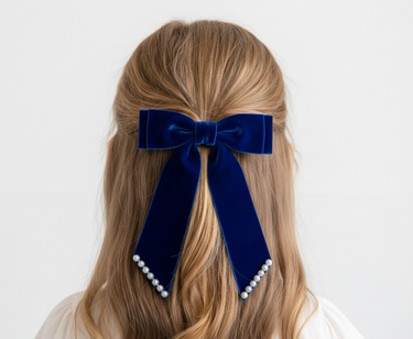 Navy blue velvet hair bow with pearl accents on a person's head against a white background