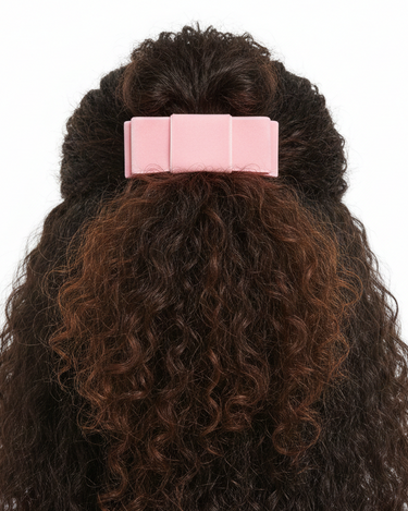 Curly hair styled with a pink barrette on a white background