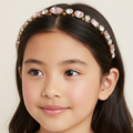 Young girl wearing a decorative headband with pink and gold elements on a plain background
