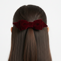 Red velvet hair bow on a person with straight hair against a white background